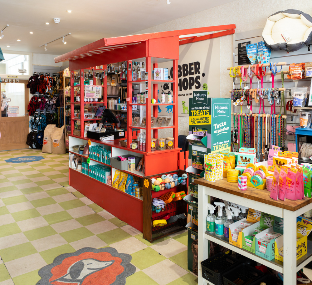 Store interior with red counter, shelves, and various products on a checkered floor.